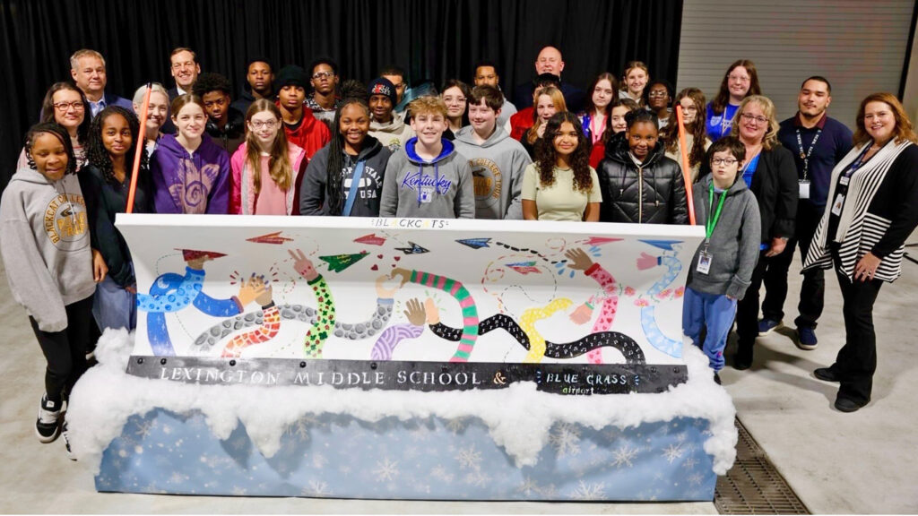 A group of students standing behind a snowplow they painted.