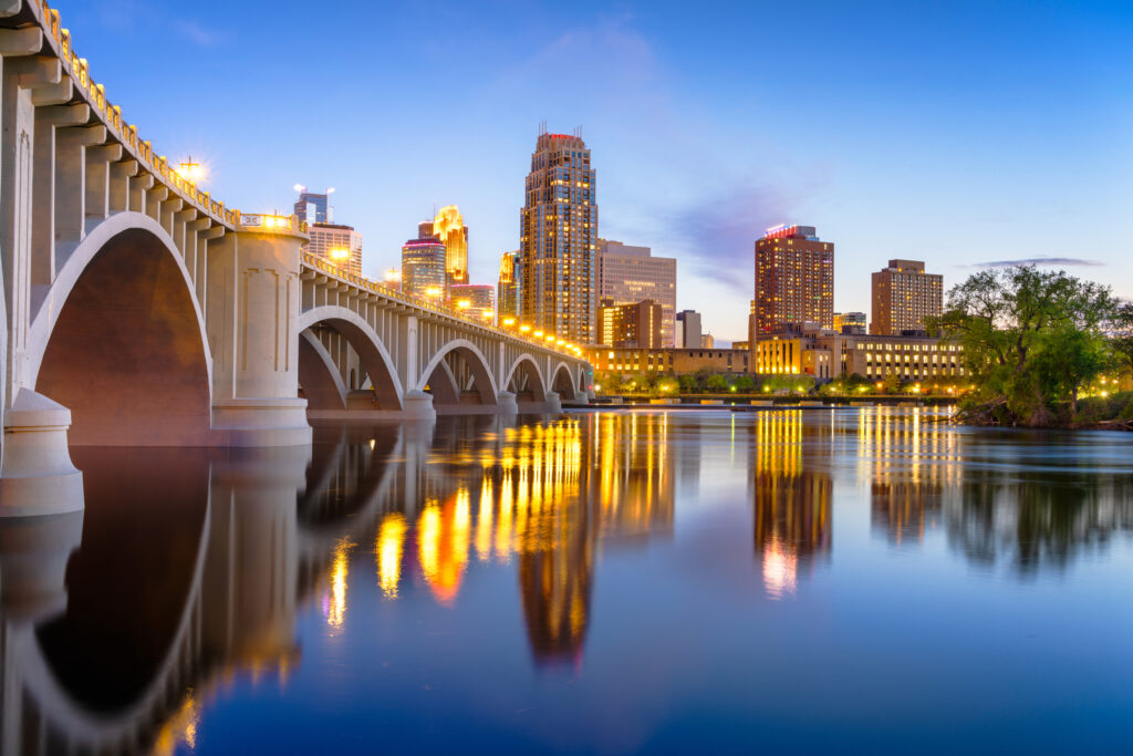 The Minneapolis skyline with a bridge over a river at twilight.
