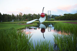 A large sculpture of a spoon with a cherry on top. The sculpture is surrounded by a small pond and grass.