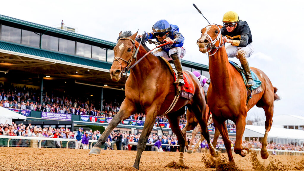 Two racehorses racing at Keeneland in front of the stands, with their jockeys.