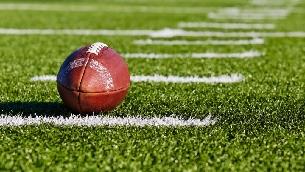 A football sitting on the turf of a football field, with the yard lines extending across the field.