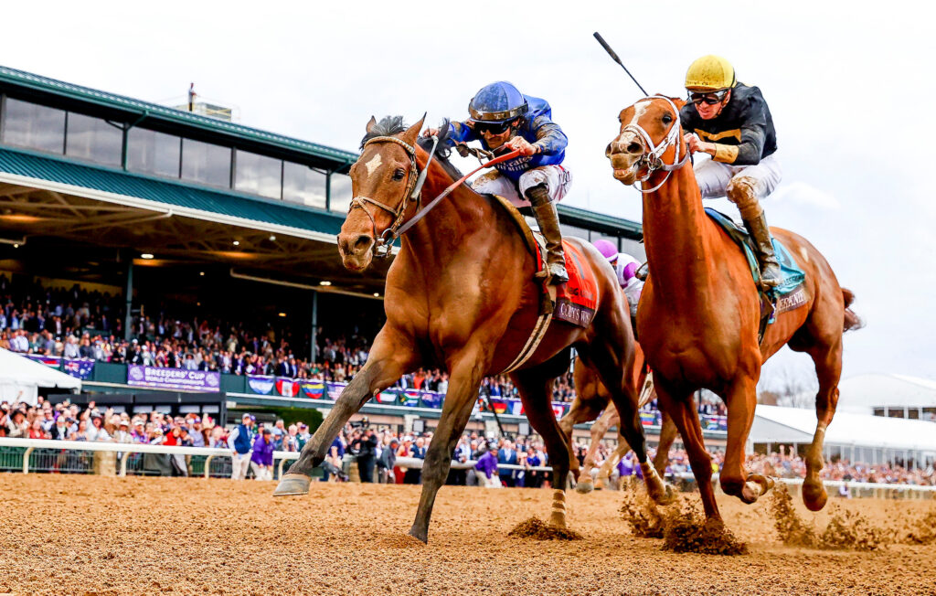 Two racehorses racing at Keeneland in front of the stands, with their jockeys.